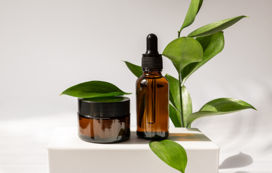 brown dropper bottle and jar on a marble block with a plant stem in the background